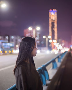 Side view of woman looking at illuminated city at night