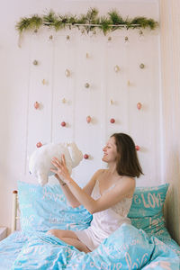 Smiling woman holding stuffed toy sitting on bed