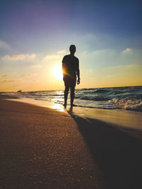 Rear view of silhouette man standing on beach during sunset