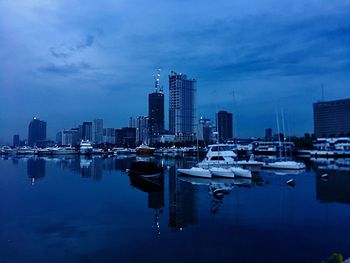 Sailboats in city by buildings against sky at dusk