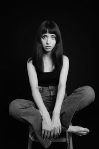 Portrait of young woman sitting on chair against black background