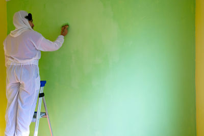 Youn man on top of a ladder is painting the wall