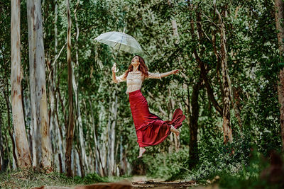 Woman with umbrella against trees in forest