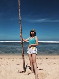 Full length of young woman standing at beach against sky during summer