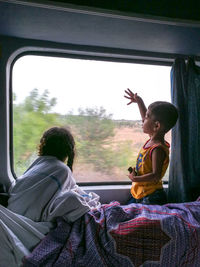Siblings looking through window while sitting in train