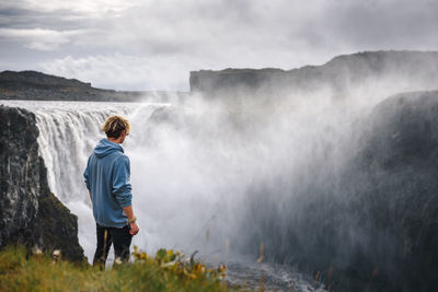 Rear view of man looking at waterfall against mountain