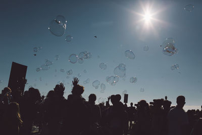 Low angle view of people and bubbles against sky on sunny day