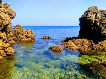 Scenic view of rocks in sea against clear sky