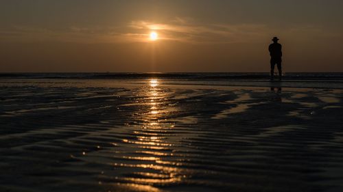 Silhouette man standing on beach against sky during sunset