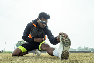 Side view of man exercising on field against clear sky