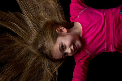 Directly above view of cheerful girl with blond hair lying on black background
