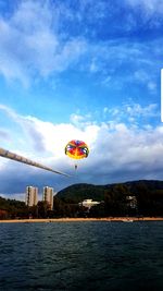 Hot air balloon flying over river in city against sky