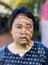 Portrait of young asian man with dappled sunlight and shadow pattern on face and clothes.