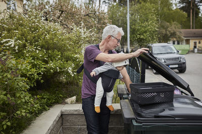 Smiling mature man with baby putting rubbish into bin