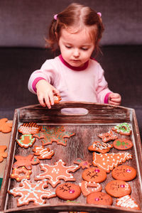 Girl placing christmas gingerbread cookies in wooden tray at home