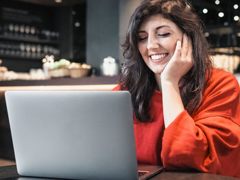 Portrait of smiling young woman using phone while sitting on table