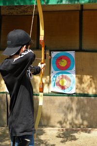 Side view of teenage boy aiming sports target with arrow