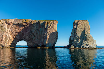 View of rock formation in sea against clear blue sky