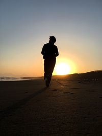 Rear view full length of woman walking at sandy beach against sky during sunset