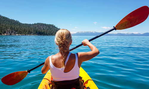 Rear view of woman rowing boat in sea against sky