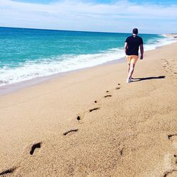 Rear view of man walking on shore at beach against sky