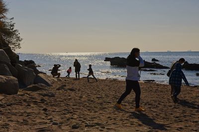 People at beach against sky during sunset