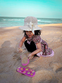Girl playing with sand at beach against sea