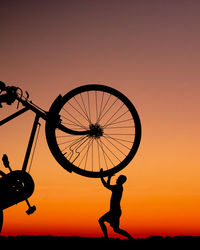 Silhouette people with bicycle against sky during sunset