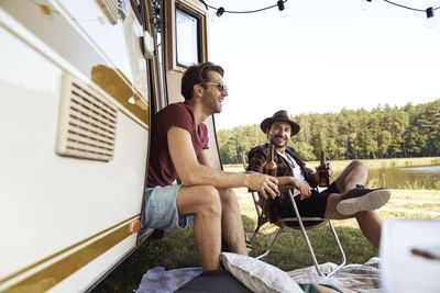 Smiling friends sitting by camper van