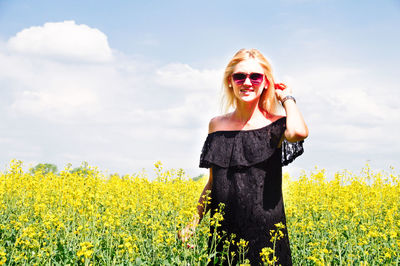 Portrait of smiling young woman standing on oilseed rape field