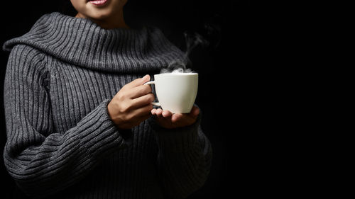 Woman holding coffee cup against black background