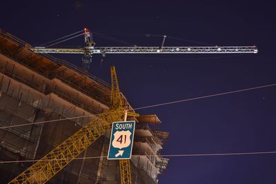 Low angle view of cranes by incomplete building against sky at night