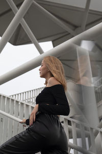 Side view of young woman sitting on railing