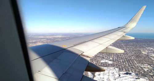 Aerial view of airplane wing over landscape against clear blue sky