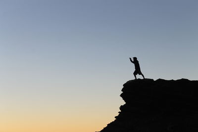 Silhouette man standing on rock against clear sky
