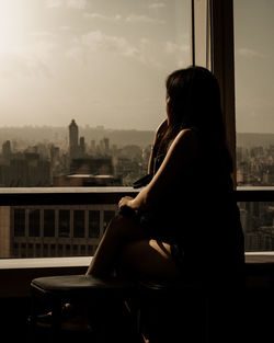 Man looking through window while sitting on railing against buildings in city