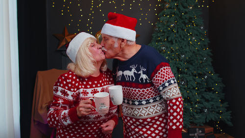 Senior couple wearing santa hat embracing at home