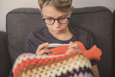 Sad boy looking at thermometer while sitting on sofa