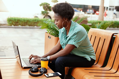 Young woman using laptop while sitting at sidewalk cafe