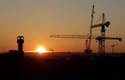 Silhouette cranes at construction site against sky during sunset