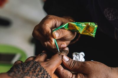 Midsection of person making henna tattoo on woman hand