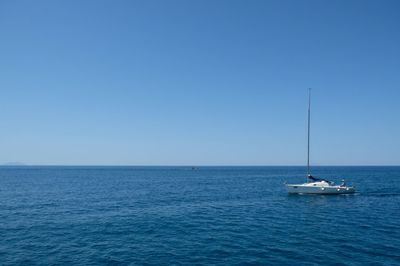 Boat sailing in sea against clear blue sky
