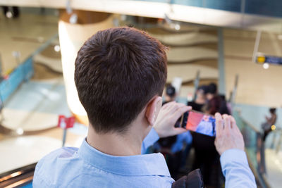 Rear view of man photographing with mobile phone at airport