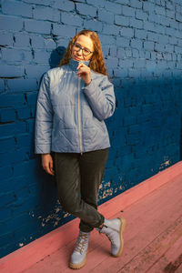 Portrait of young woman standing against wall