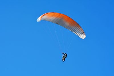 Low angle view of paragliding against clear blue sky