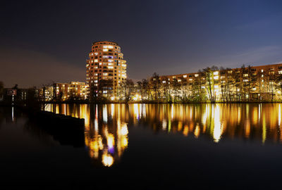 Illuminated buildings by river against sky at night