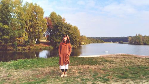 Portrait of young woman standing by lake against sky