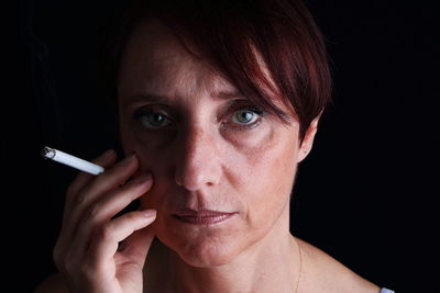 Close-up portrait of mature woman with cigarette against black background