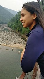 Side view of smiling young woman standing on mountain against sky