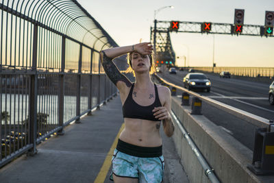 Young tattooed woman running on bridge with sunset behind